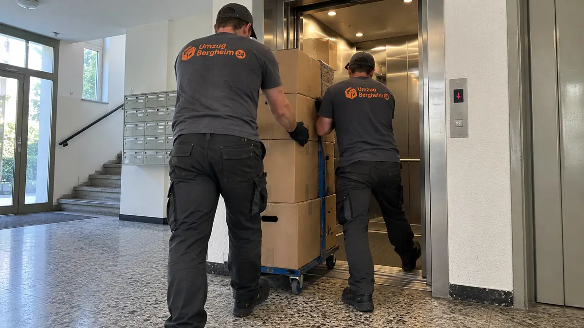 Wohnungsumzug Bergheim: zwei Umzugshelfer schieben einen Rollwagen mit Kartons in den Aufzug eines Wohnhauses